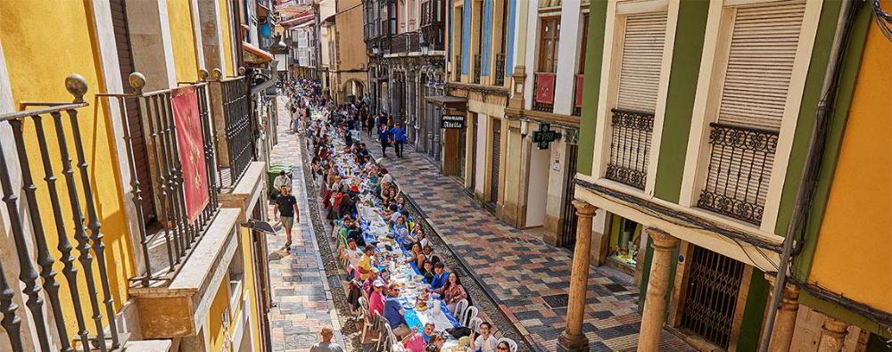 Foto del día del Bollo en Avilés. Una larga mesa que recorre las calles con la gente comiendo