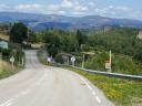Ancha carretera de montaña con quitamiedos rodeada de colinas verdes boscosas
