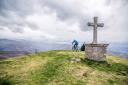 Ciclista junto a una gran cruz de piedra en una cima montañosa nublada