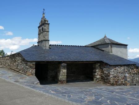 Iglesia rústica de piedra con tejado de pizarra y espadaña bajo un cielo despejado