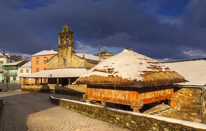 Vista di Samartín, capoluogo del comune di San Martín de Oscos, in una giornata invernale. Vediamo una chiesa in pietra, con il suo campanile, che domina la piazza principale del villaggio e, accanto ad essa, un tradizionale hórreo in legno, con i tetti coperti da una coltre bianca di neve, che aggiunge un tocco rustico e pittoresco.