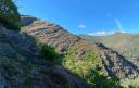 A path between hills and mountains covered with vegetation under the blue sky.