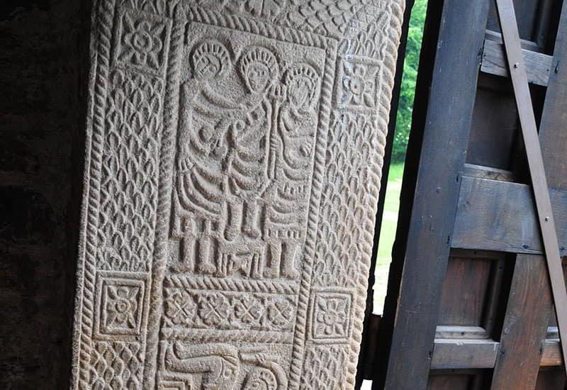 Relevo pré-românico da ombreira de San Miguel de Lillo, com desenhos de cenas esculpidas geometricamente.