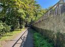A couple of hikers walking along a path between a stone wall and a wooden fence.