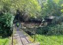 Hiker crossing a wooden bridge over a river on the Baltasara Railway route.
