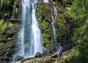 A Seimeira waterfall in full fall, with hikers contemplating it from the rocks.