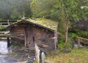 Small stone building with slate roof, covered with moss by the stream.