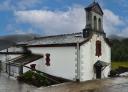 Iglesia de Doiras, templo blanco con espadaña y detalles en rojo, en entorno rural.