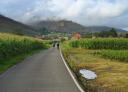 Dos senderistas cruzando camino entre maizales y pueblos asturianos