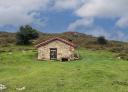 Small stone hut with gable roof in mountain meadow