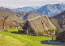 Braña Tuiza with a hut with a vegetation roof and snow-capped mountains in the background.