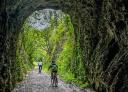 Ciclistas cruzando túnel rodeado de vegetación en la Vía Verde del Eo