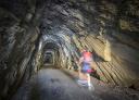 Senderista cruzando túnel excavado en roca en la antigua vía del tren