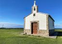 Ermita en una pradera verde con vistas al mar.