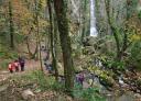 Families look at the river and the waterfall amidst lush autumn vegetation.