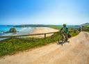 Two cyclists ride along a path while contemplating a panoramic view of Peñarronda beach.