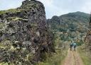 Pareja de senderistas caminando entre grandes paredes de roca escarpadas y vegetación