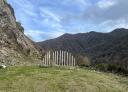 Vehicle access cut by vertical wooden posts in a hilly landscape