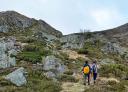 Hikers on a rocky path through scrubland and rocky mountains