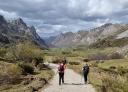Two people walk along a wide path in a mountain valley.