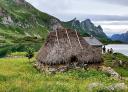 Old stone hut with thatched roof by a lake in a green, hilly valley