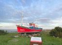 Decorative red fishing boat stranded in the grass with information sign in front and the amr in the background
