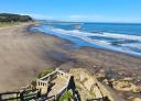 View from the top of a wide beach with wooden stairs and waves crashing on the shore.