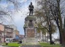 Estatua de bronce de un hombre de pie sobre un pedestal, rodeada de árboles