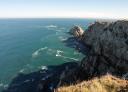 Vue aérienne de la côte rocheuse avec des falaises abruptes et des vagues se jetant dans la mer bleu-vert.