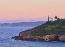 Lighthouse on the top of a rocky cliff at sunset with calm seas