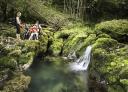Cascada rodeada de exuberante vegetación verde con una familia sentada junto al agua