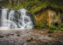 Imponente cascada de agua cayendo al lado de un antiguo molino de piedra