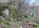 Hiker walking along a path in the middle of the forest, leaving behind a semi-reduced stone building.
