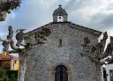 Antigua Capilla de piedra con campanario al final de una calle con árboles a ambos lados