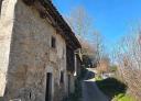 Old stone house with wooden windows along a road in a rural and hilly environment.