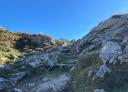 Path forming a staircase with stones and markings on a rock indicating a mountain path.