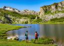 Two people contemplate the water of a lake with the Picos de Europa in the background.