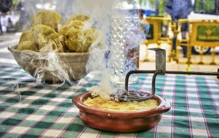 Arroz con leche asturiano siendo requemado con hierro tradicional, con humo visible; al fondo, limones, una botella de anís y mantel de cuadros