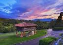 Traditional Asturian granary with a red tile roof in the middle of a paved path surrounded by vegetation.