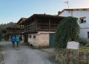 Two people walk through an Asturian village with stone houses and hórreos (raised granaries).