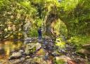 Hiker walking over rocks to a natural cave with vegetation-covered rock formations.