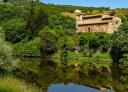 Traditional stone church next to a river, surrounded by lush green vegetation.