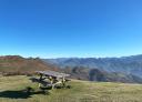 Mesa de picnic de madera en una amplia campa verde y montes de fondo bajo el cielo azul