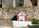 Pequeña fuente de piedra blanca y roja con una cruz de color rojo