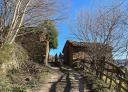 Dos senderistas ascienden por un camino rural entre casas de piedra tradicionales