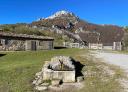 Fuente de piedra con construcción rural de piedra y montañas al fondo