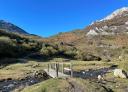 Pasarela de madera cruza un río, ofreciendo un sendero llano con montes al fondo