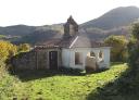Small stone chapel with a bell tower, surrounded by lawns and mountains in the background.