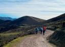 Group of hikers walking along a wide dirt track in a mountainous environment.