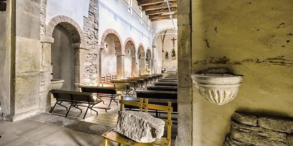 Vista da nave da igreja de Santiago de Gobiendes, mostrando em primeiro plano os pilares, os arcos e a pia batismal.